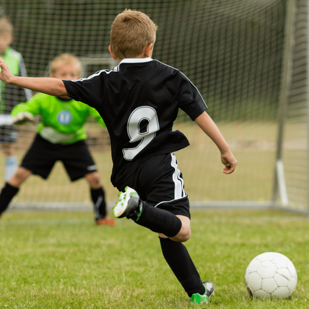 young childkicking a soccer ball on soccer field