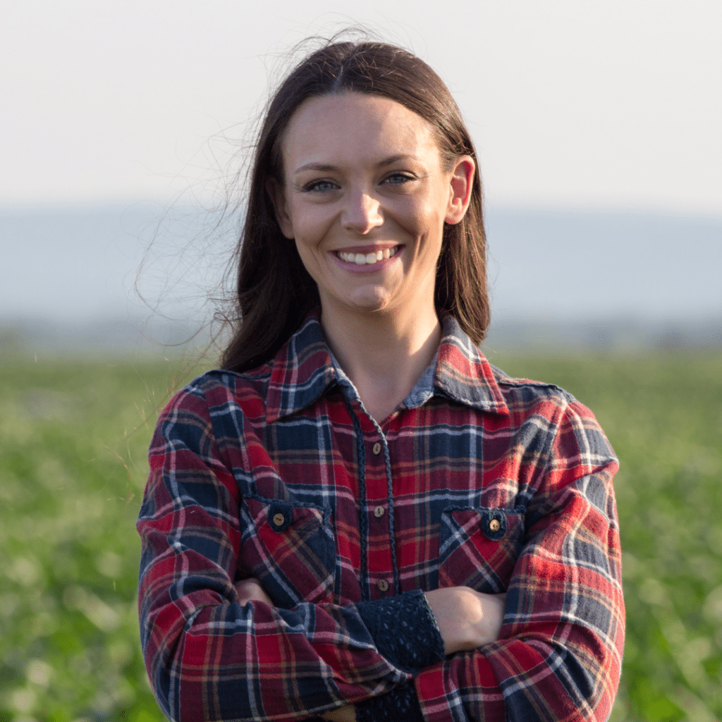 happy female patient of Doc Blackstone standing in a fiekd with arms crossed wearing plaid shirt