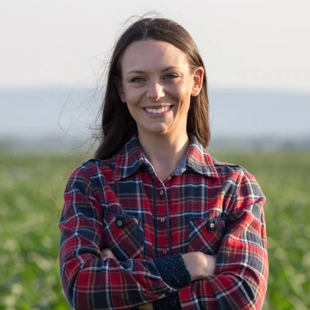happy female patient of Doc Blackstone standing in a fiekd with arms crossed wearing plaid shirt