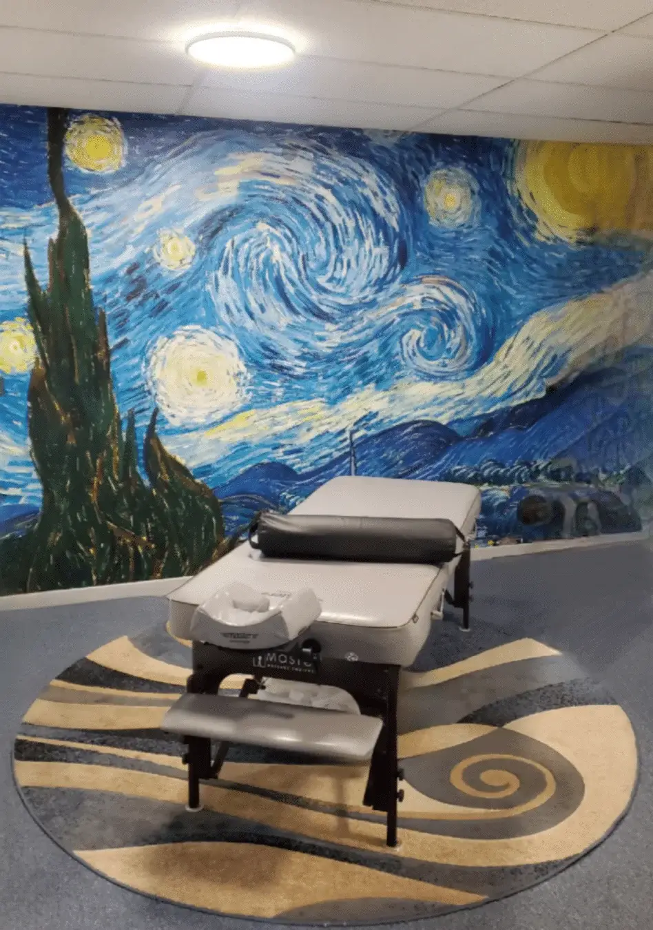 Massage therapy table in well lit therapy room with "starry Night' accent wall by Van Gogh
